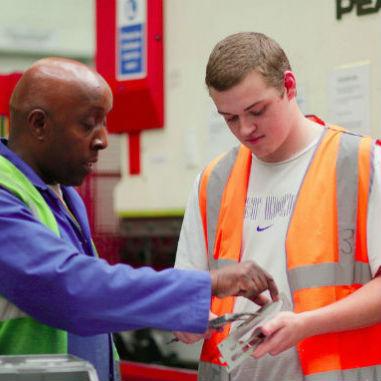 Image shows a man explaining a metal part to an apprentice