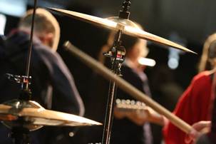 Image shows cymbals and high hats as part of a drum kit, with a drum stick being held in the air