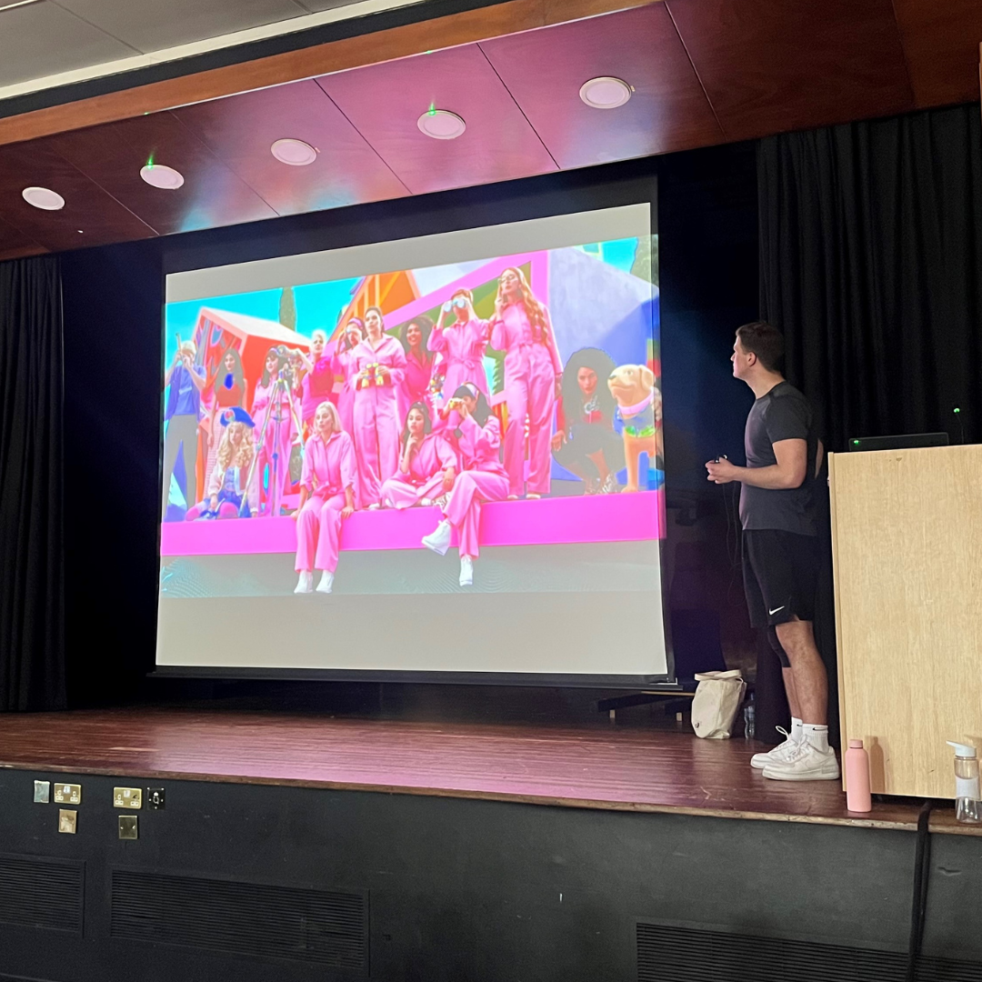 Image shows Richard Womersley on stage talking the pupils through a scene from the Barbie movie