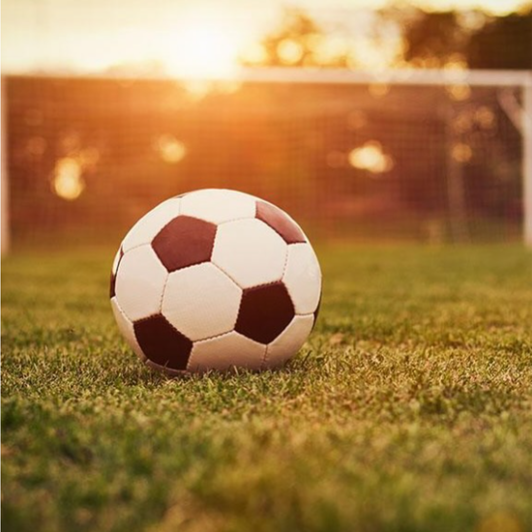 Image shows a football on a pitch at sunset