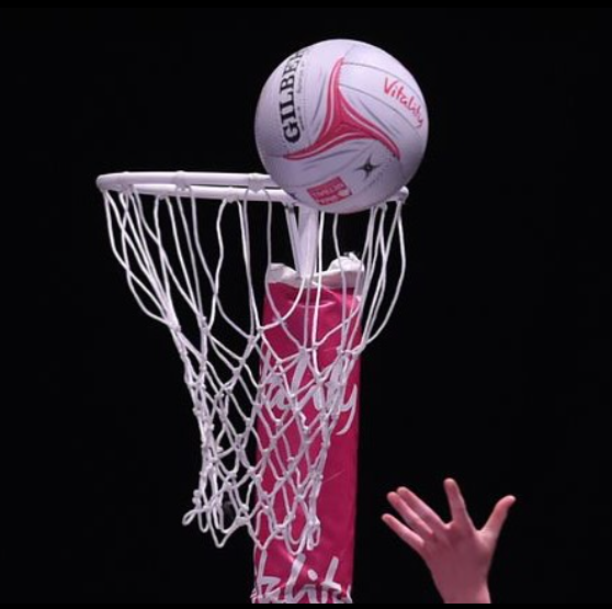 Image shows a hand aiming a netball towards the hoop against a black background.