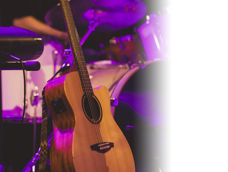 Image shows an accoustic guitar leaning against a drum kit