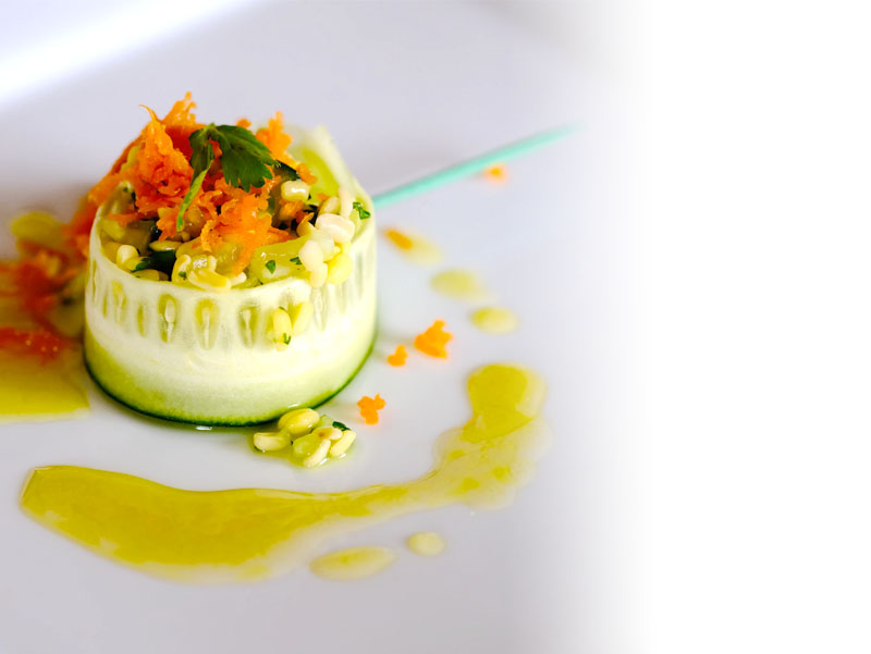 Image shows a plated disn of rice, and herbs, surrounded by a thin slice of courgette and topped with grated carrot, The plate has been drizzled with sauce.