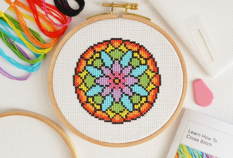 Image shows embroidery canvas in a hoop with a cross stitched circular design