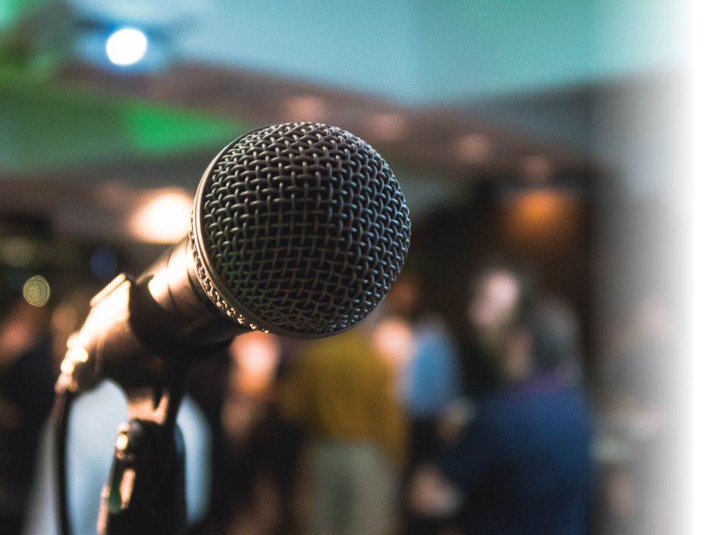 Image shows a microphone in focus with a blurred crowd and awnings behind it